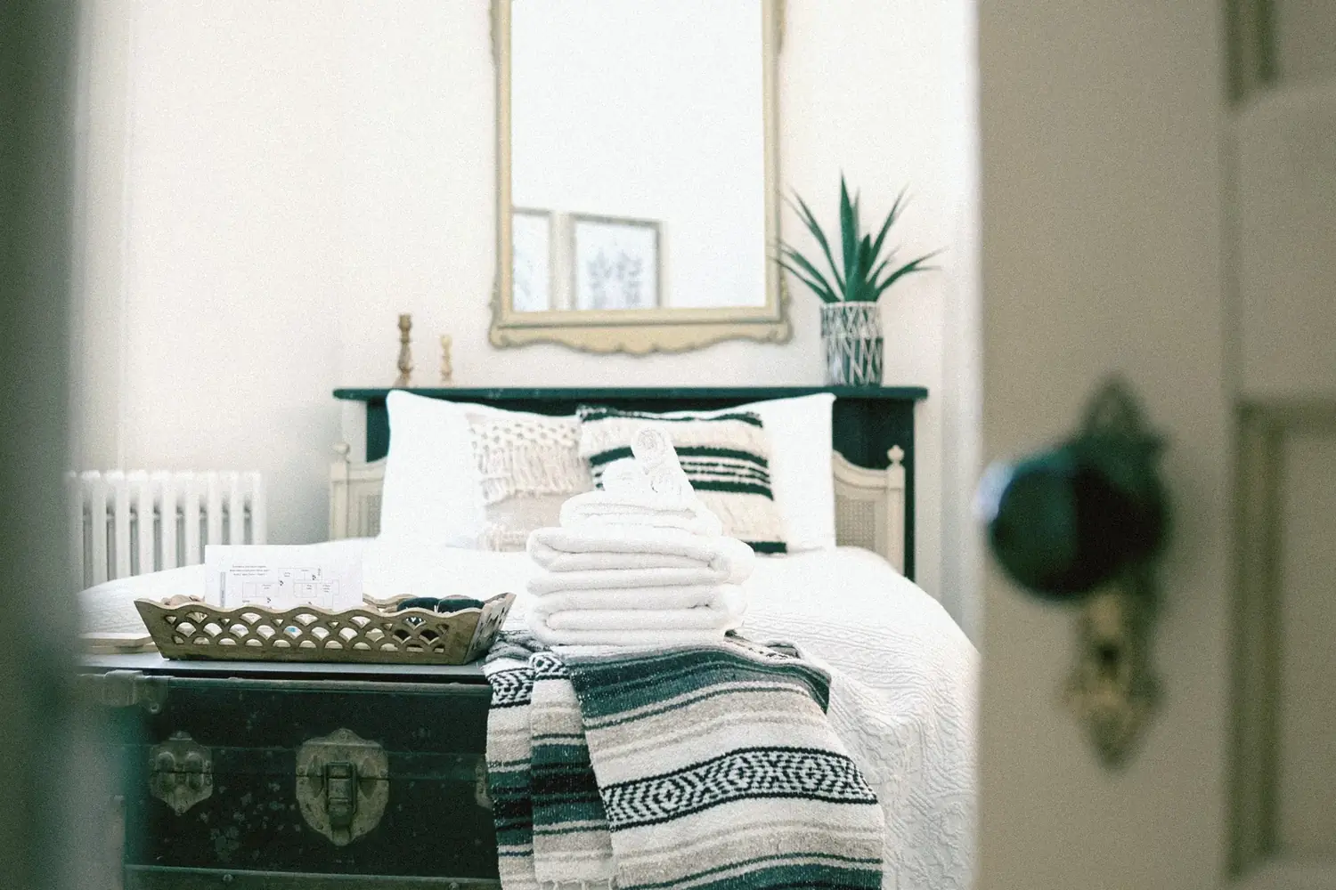 Bedroom at The Old Ruth through the doorway with trunk and folded towels — turnkey furnished housing