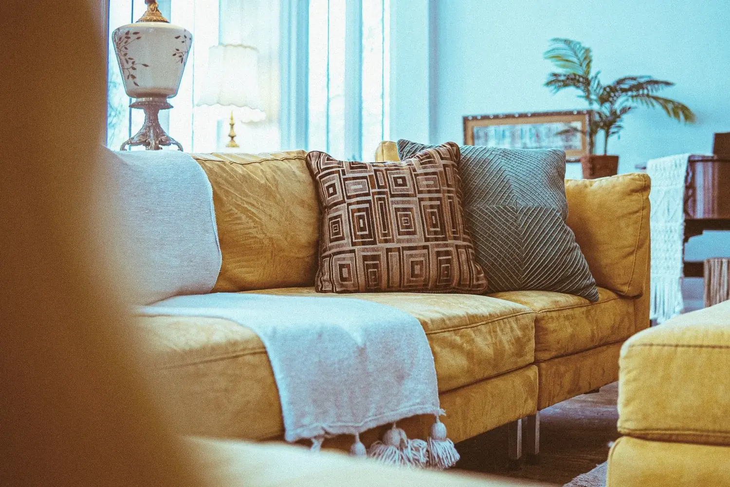 Mustard sofa with layered pillows and bright windows in a furnished common room at The Old Ruth